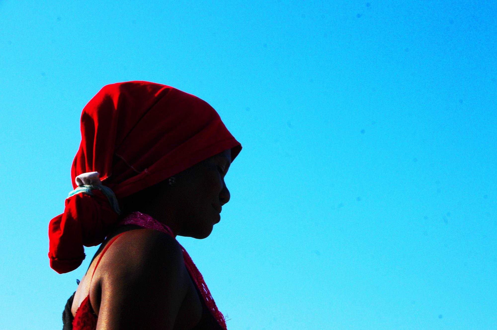 A woman in a red headwrap seen in profile against a bright blue wall, Cartagena, Colombia — photograph by Brian Walker