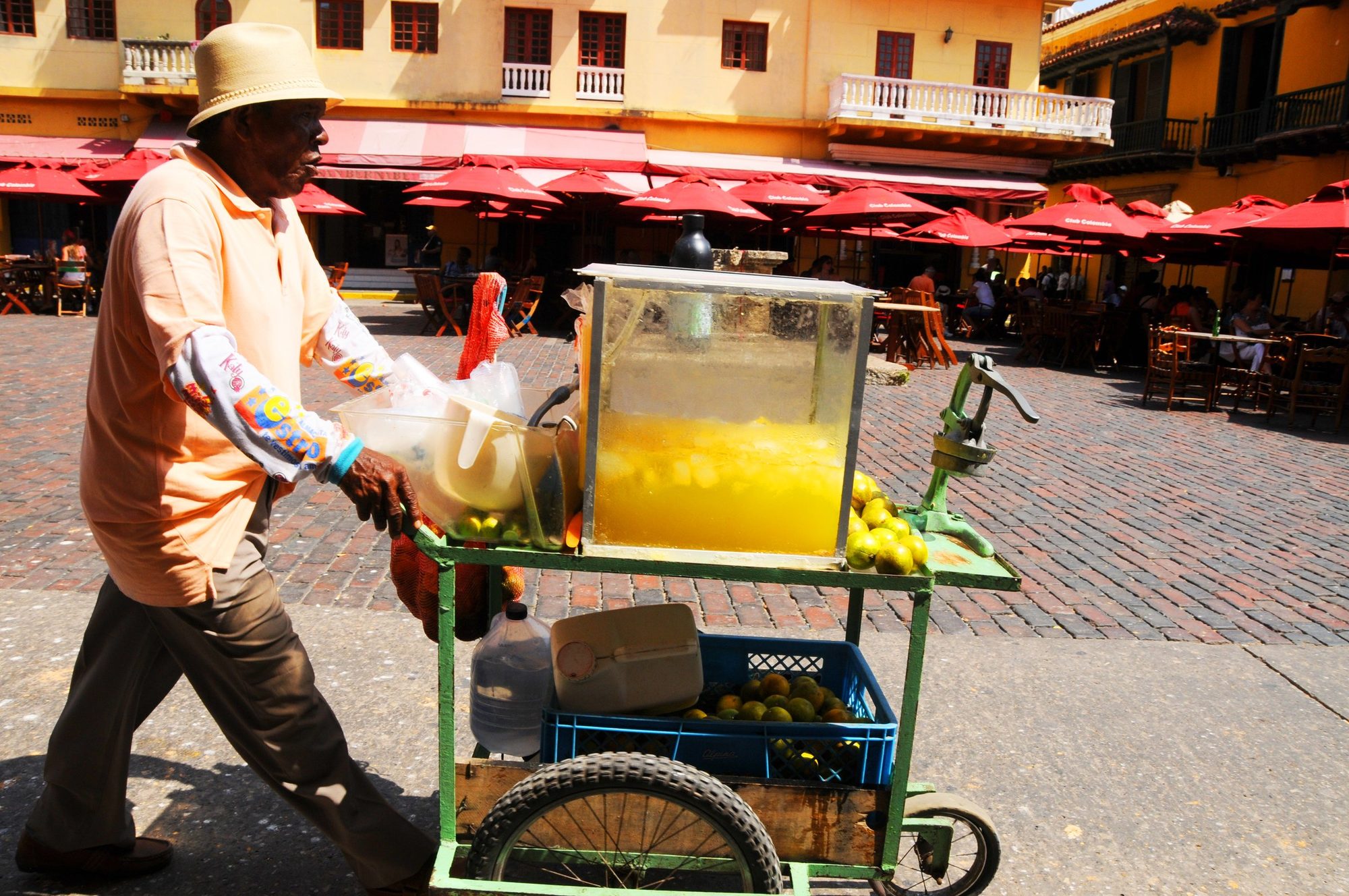A street vendor pushing a glass-fronted fruit cart across a market square, Cartagena, Colombia — photograph by Brian Walker