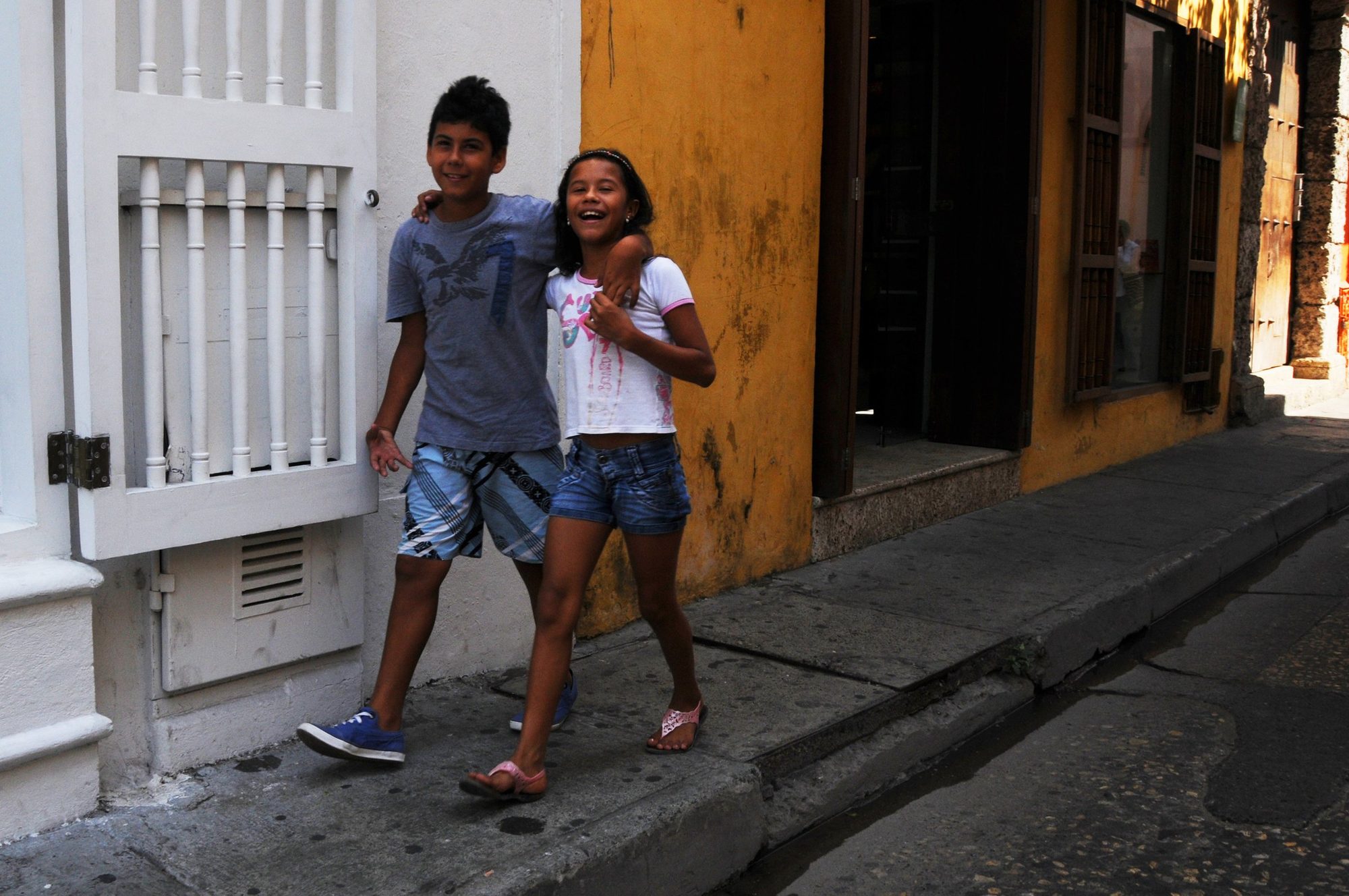 Two children standing together in a narrow sunlit street, Cartagena, Colombia — photograph by Brian Walker