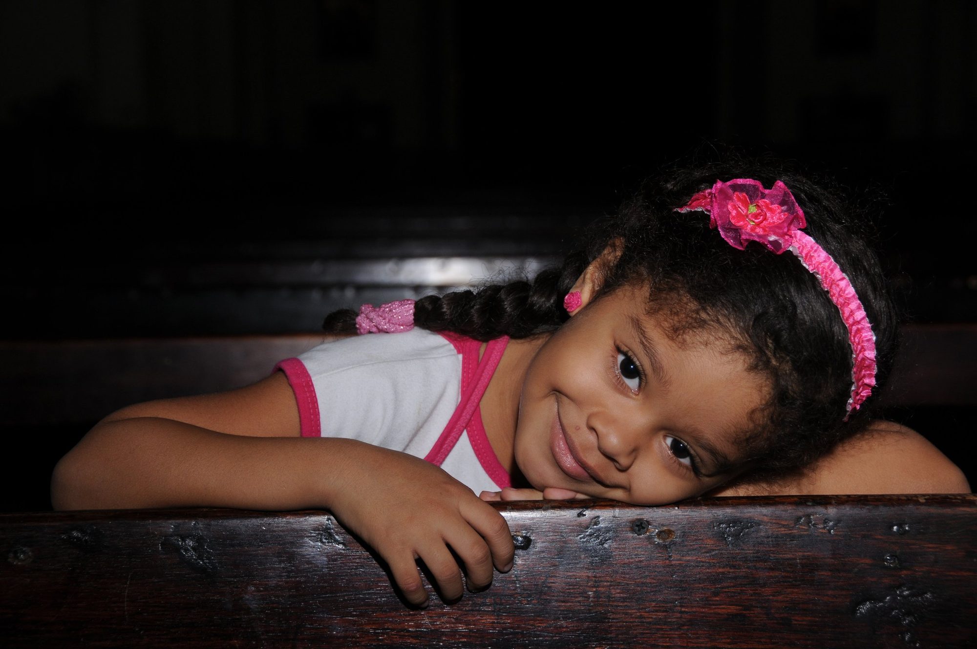 A young girl in a pink headband resting her arms on a wooden rail, smiling, Cartagena, Colombia — photograph by Brian Walker