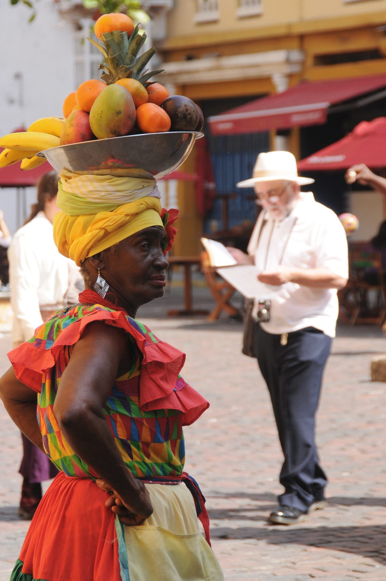 A palenquera in a ruffled dress carrying a bowl of fruit balanced on her head, Cartagena, Colombia — photograph by Brian Walker