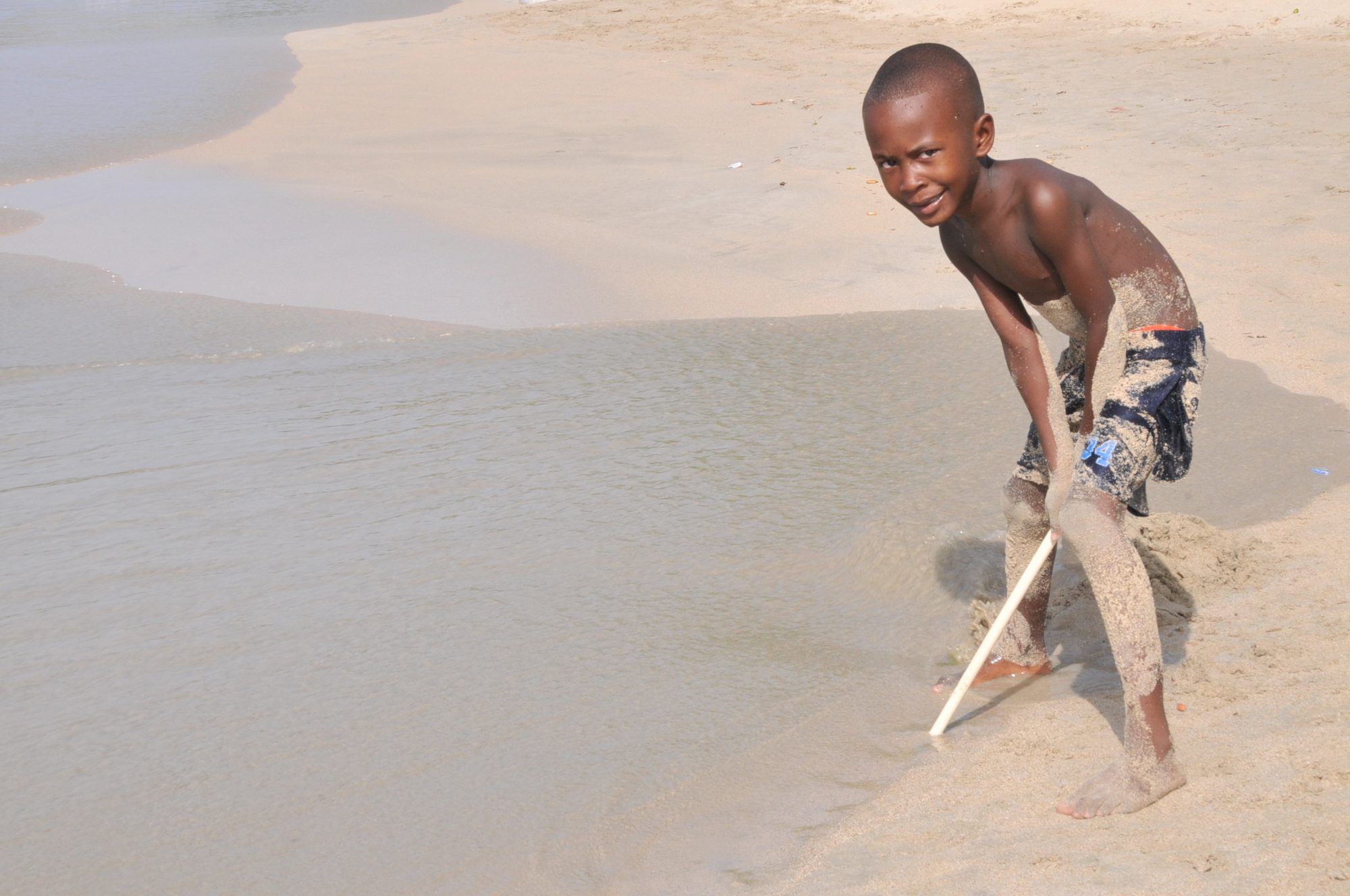 A boy dragging a stick through the wet sand at the water's edge, Saint Vincent — photograph by Brian Walker