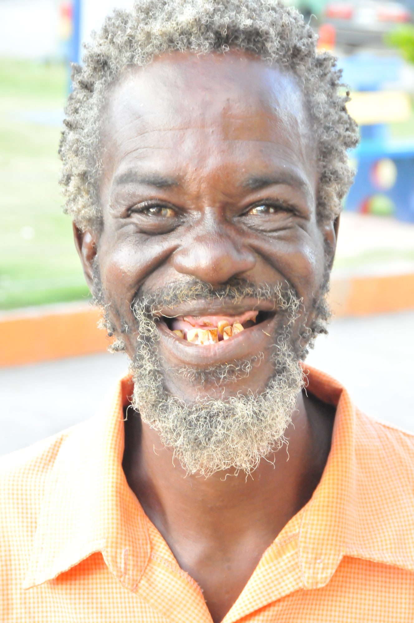 Close portrait of a smiling older man with a grey beard in an orange checked shirt, Saint Vincent — photograph by Brian Walker