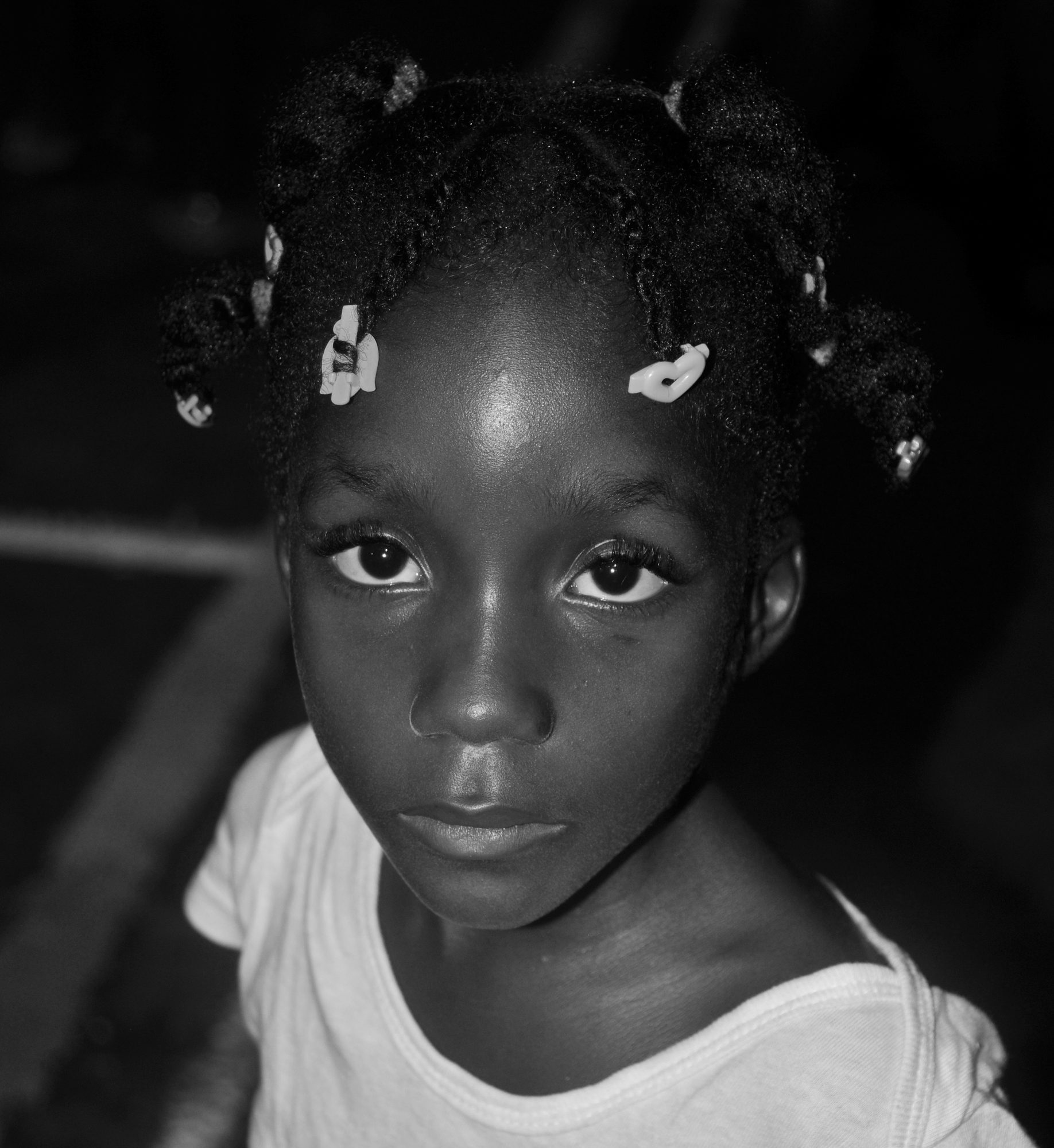 Close portrait of a girl with beaded braids looking straight at the camera, black and white — photograph by Brian Walker