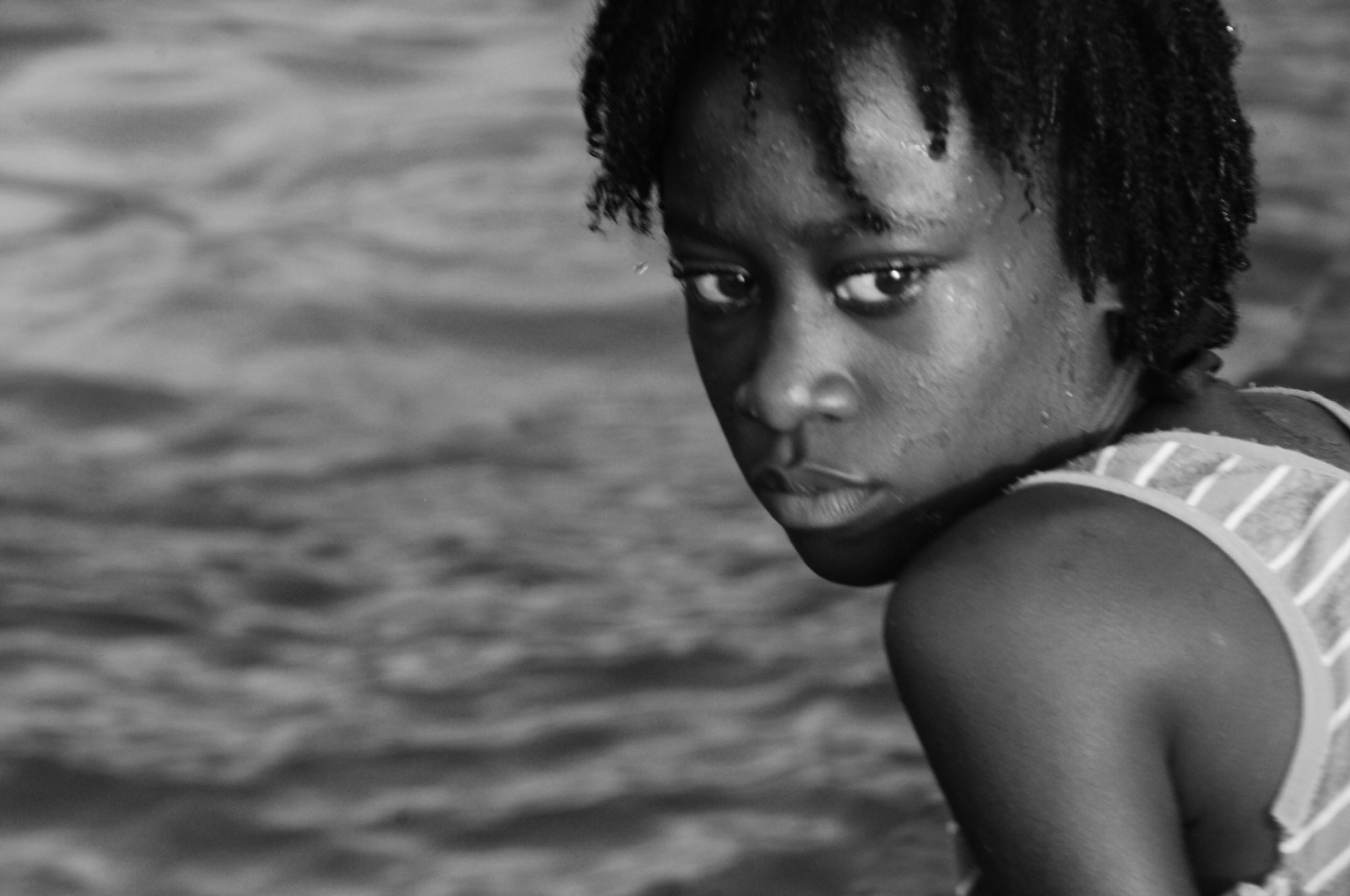 A girl turning to look back over her shoulder, open water behind her, black and white — photograph by Brian Walker